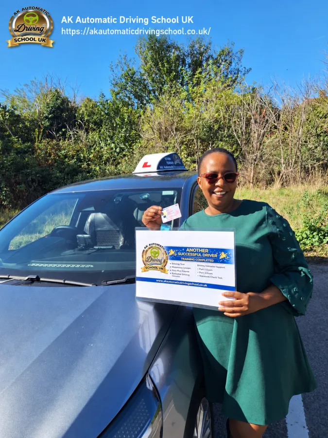 AK Automatic Driving School student holding a driving licence and a training completion sign beside the instructor car