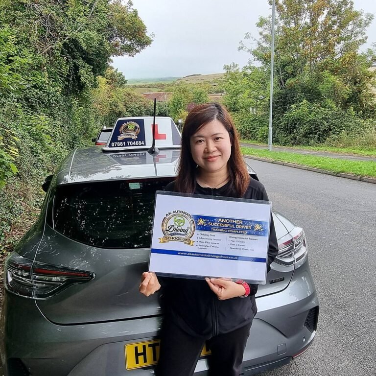 Smiling AK Automatic Driving School pupil holding an 'Another successful driver' training completed sign beside the automatic training car